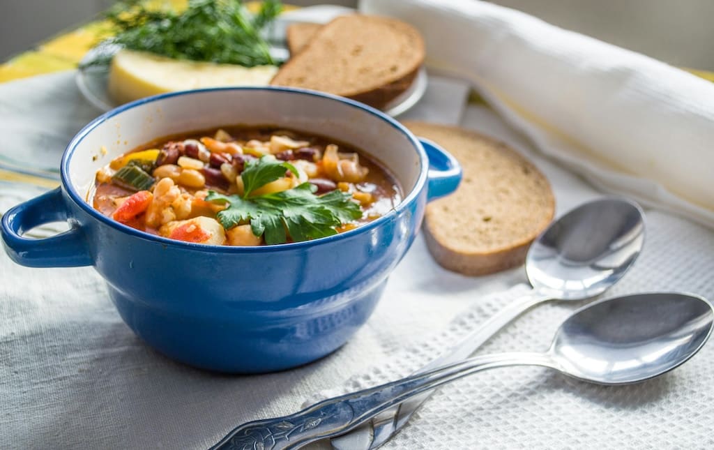 Italian soup in blue bowl on white tablecloth with spoons and bread