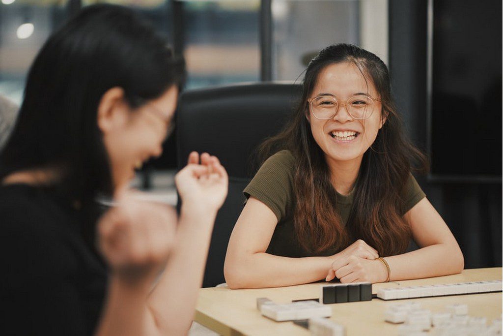 Two Asian women laughing while playing a game together Two women laughing with each other at a desk