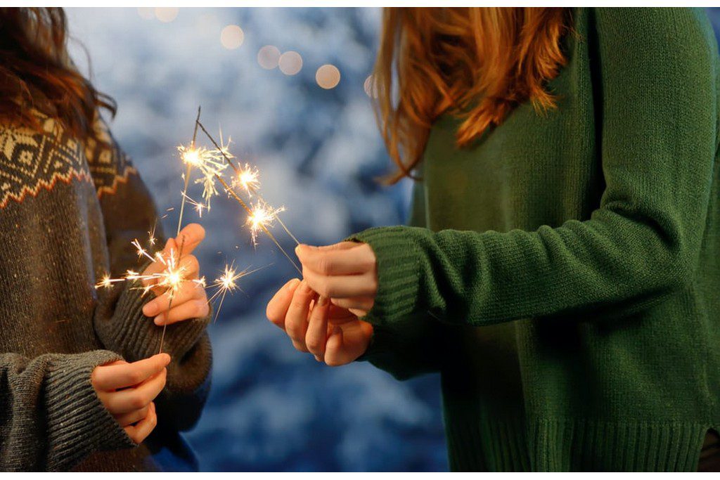 Two White women holding sparklers while wearing green sweaters Two women in green sweatshirts holding sparklers
