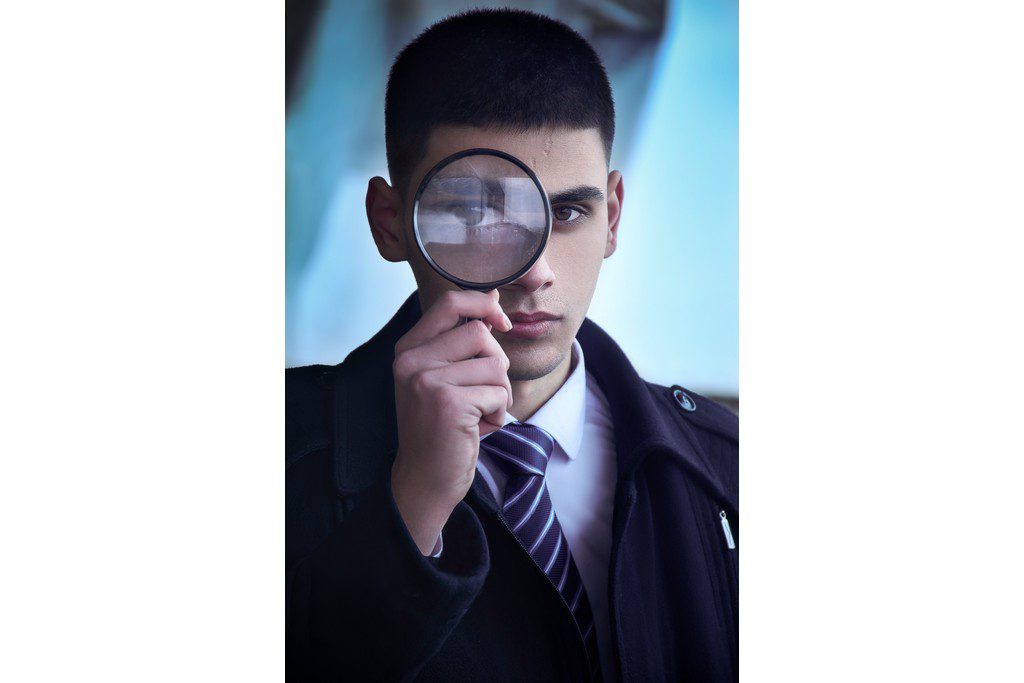 A Latino man looks through a magnifying glass kid making a detective pose