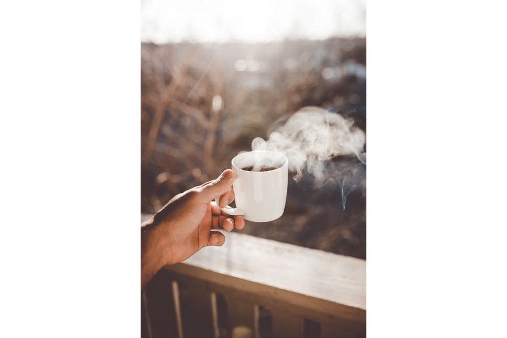 A person holding a steaming cup of coffee outdoors coffee cup on a fall morning