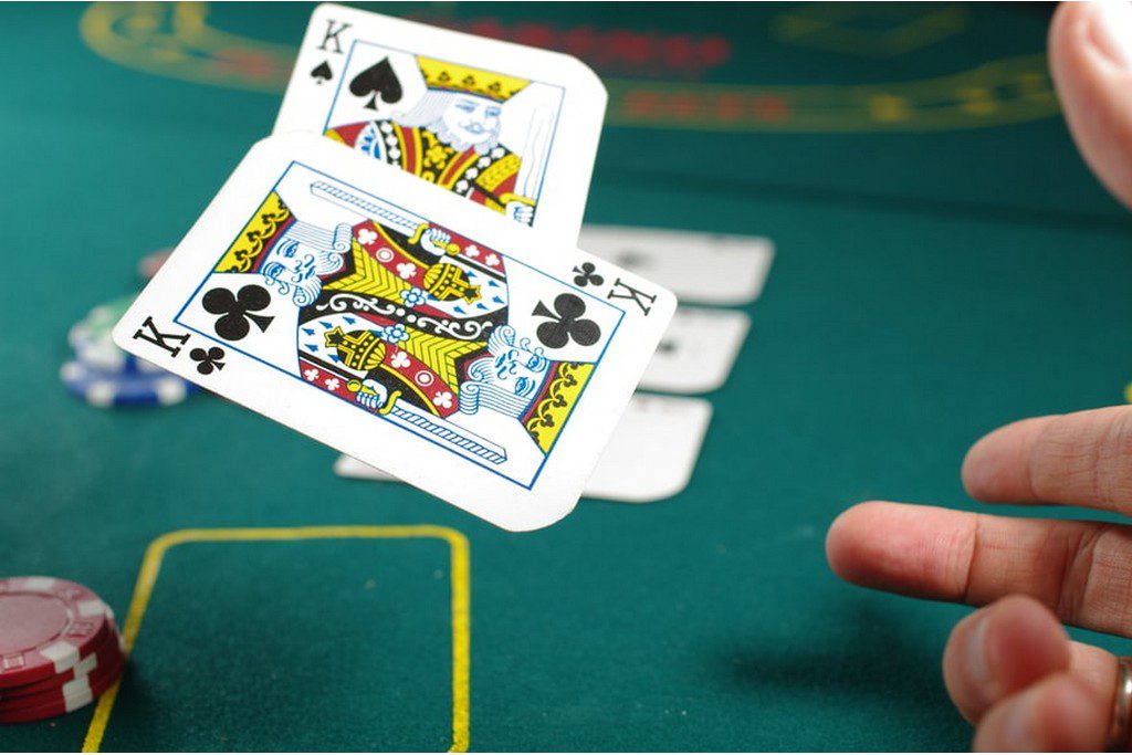 Two playing cards being tossed on a table man folding his blackjack cards