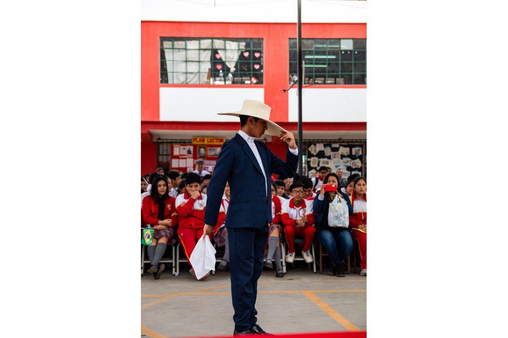 A Latino man dancing in the center of a large room with spectators man in a cowboy hat addressing the crowd