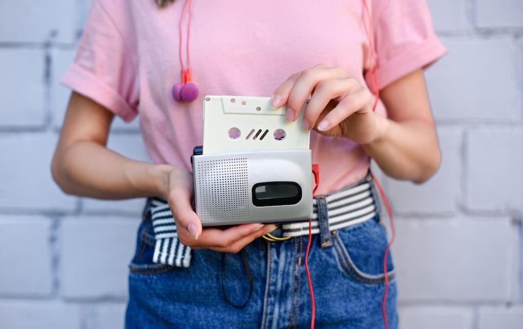 cropped shot of woman with earphones holding retro cassette player and audio cassette in hands