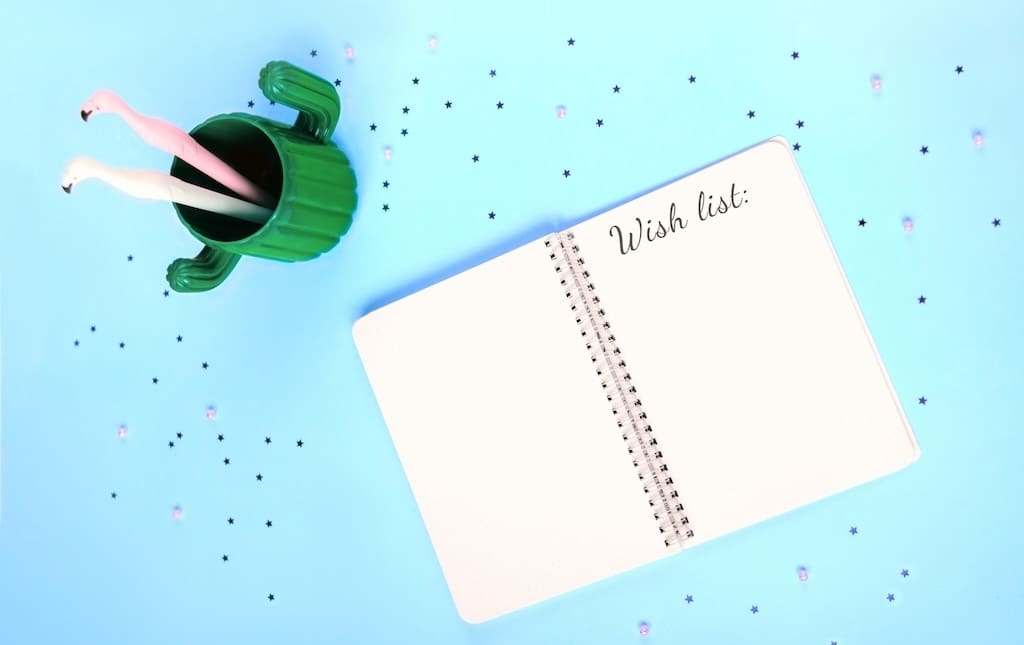 Notebook open to a page that says wish list on a blue table