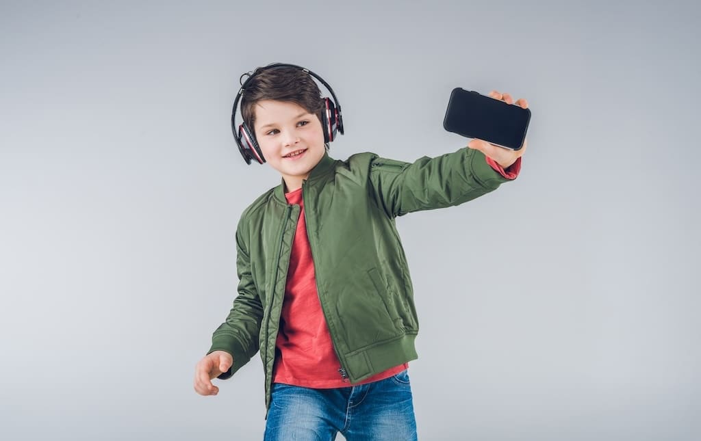 Cute boy with headphones taking selfie isolated on grey