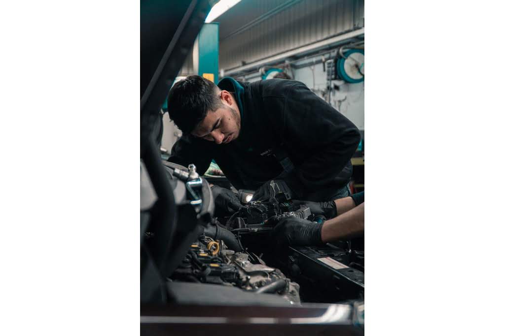 A Caucasian boy looking at the inside of a car engine mechanic working