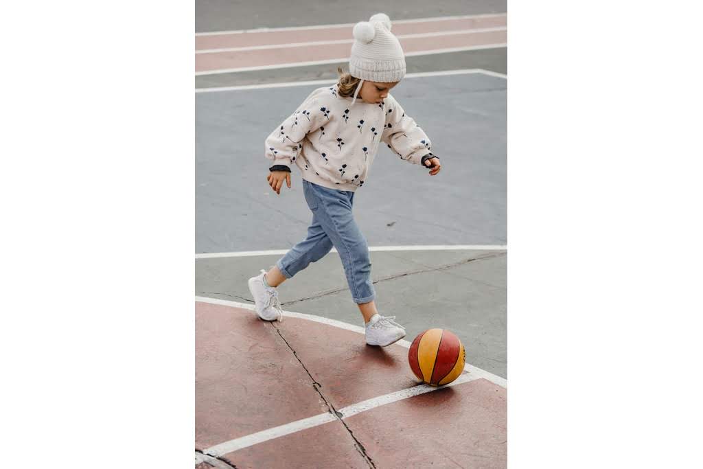 A Caucasian girl kicking a ball on a basketball court kid play8ing basketball