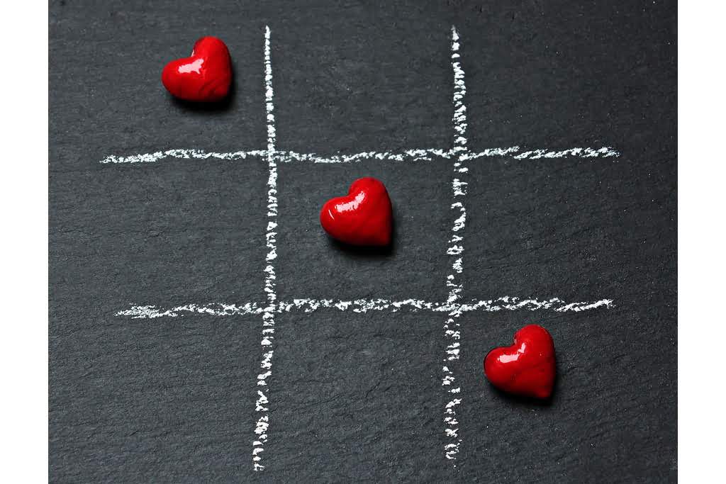 A chalkboard with a tic tac toe grid with red hearts in a diagonal tic tac toe