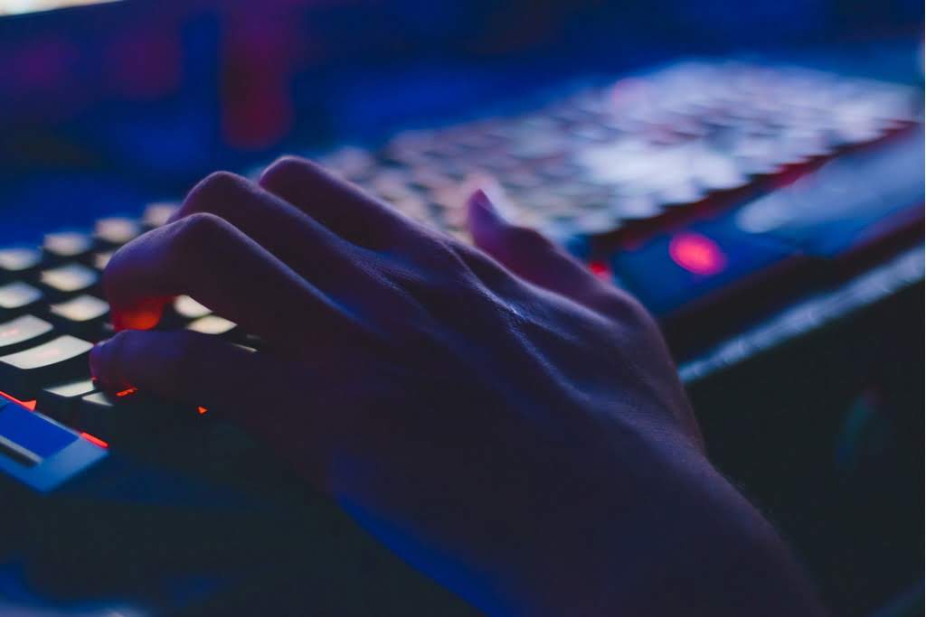 A hand typing on a backlit keyboard light up keyboard
