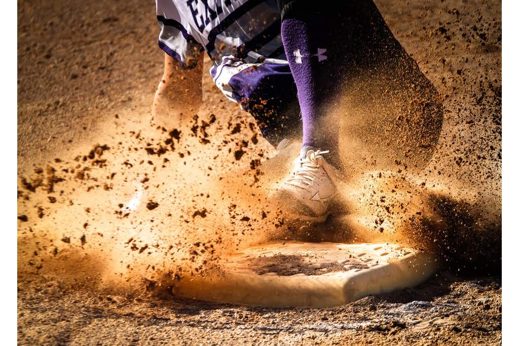 A White person sliding into a baseball base with dirt flying everywhere sliding to first base