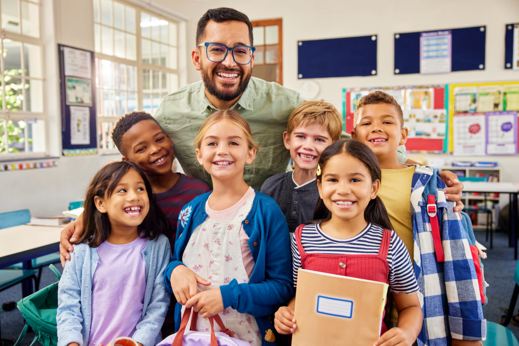 Elementary school kids stand smiling in class with their teacher