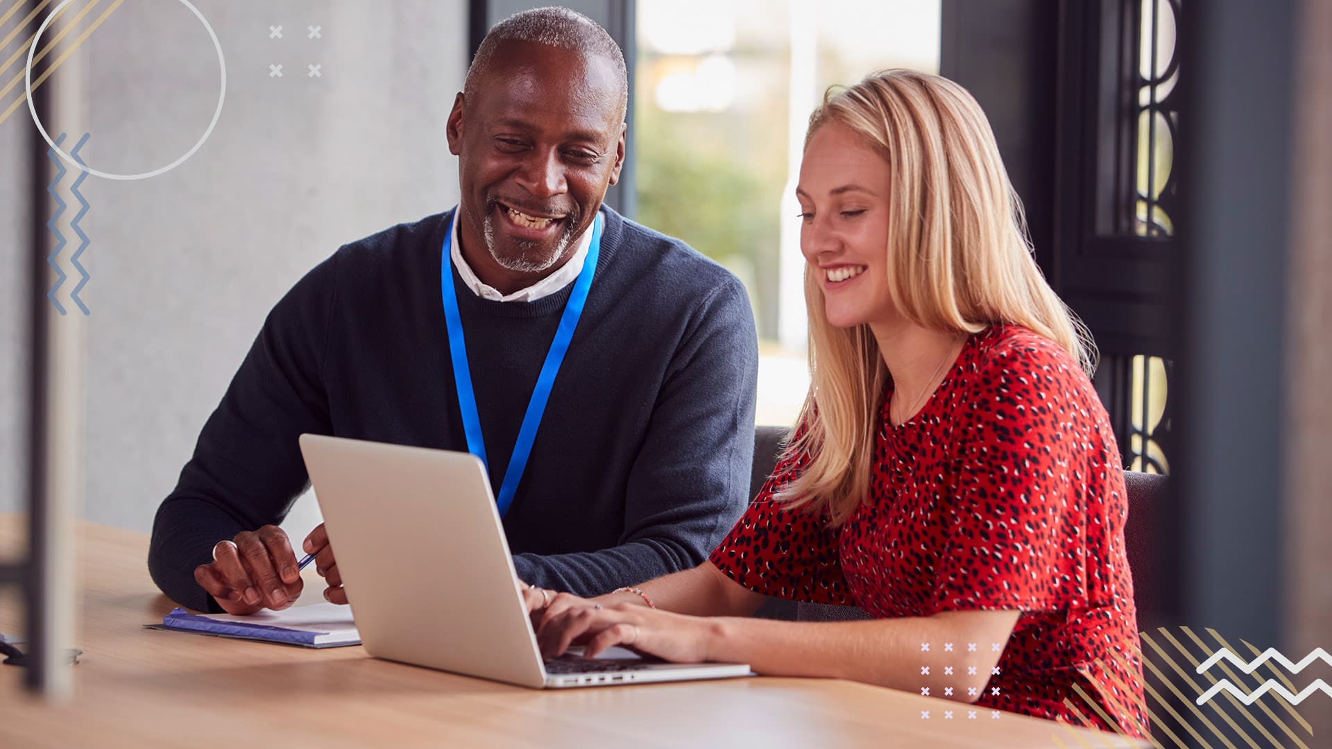 Two smiling PTA members sitting at a table looking at an open laptop.