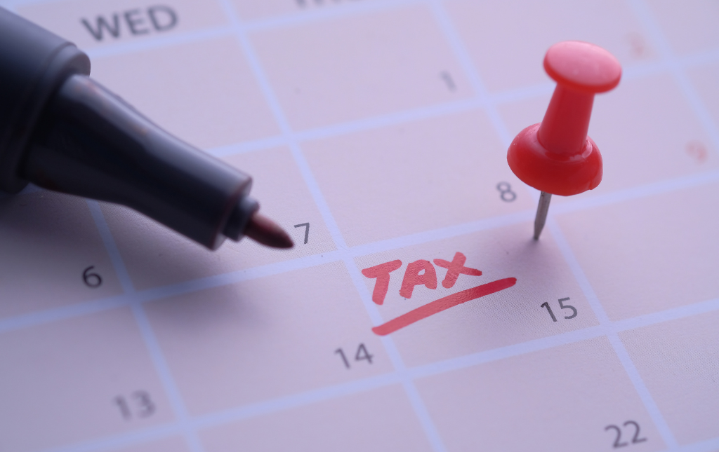 Calendar with "Tax" written in red on the 15th of the month beside a marker and a thumbtack.