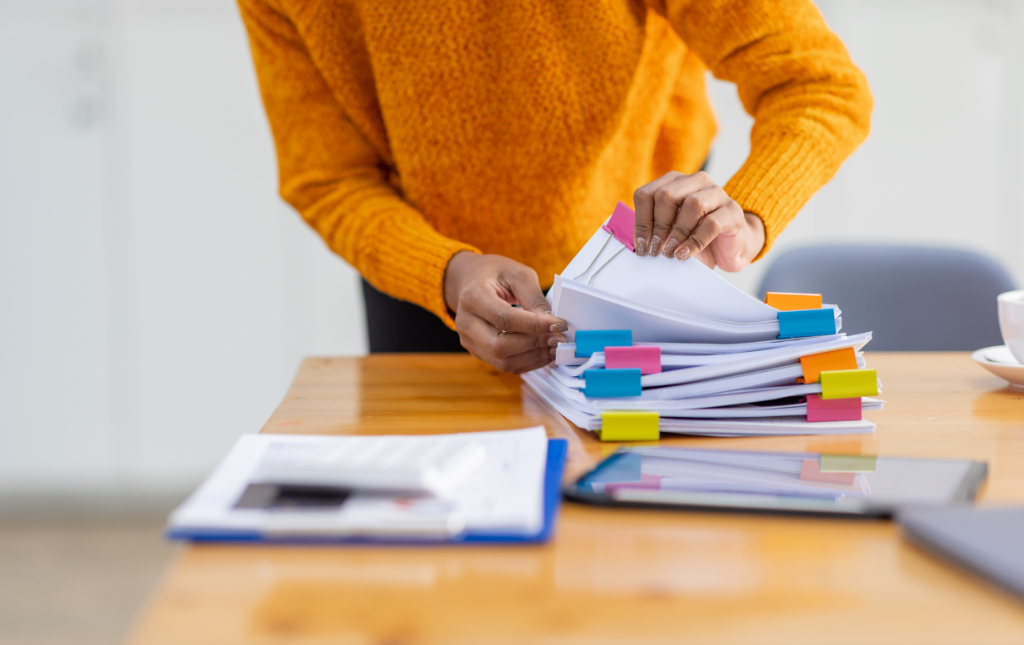 A person standing by a desk, sorting through a pile of documents.