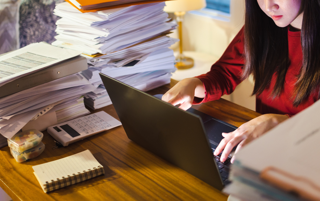 Woman at a computer surrounded by documents, a notepad, and a calculator.